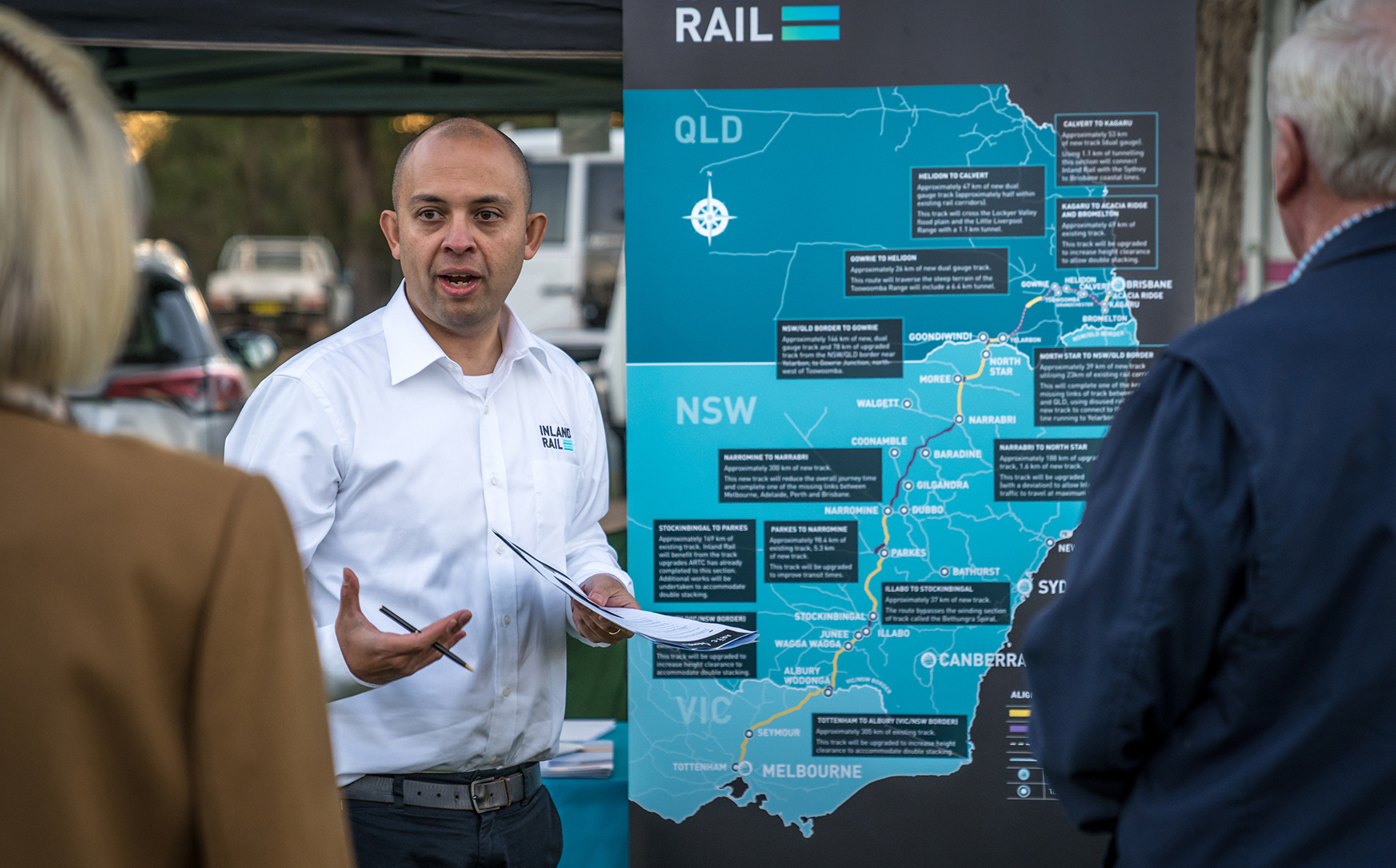 A man standing in front of a map of Inland Rail talking to two people