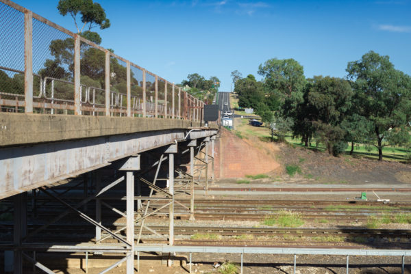 A rusty road bridge passes over railway tracks.