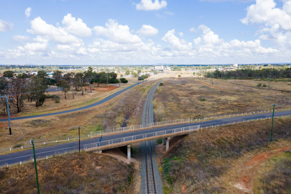An aerial shot of a rail line travelling under a road bridge.