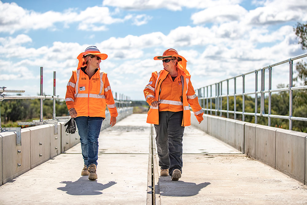Two rail workers dressed in PPE walking on a bridge - rail jobs Australia