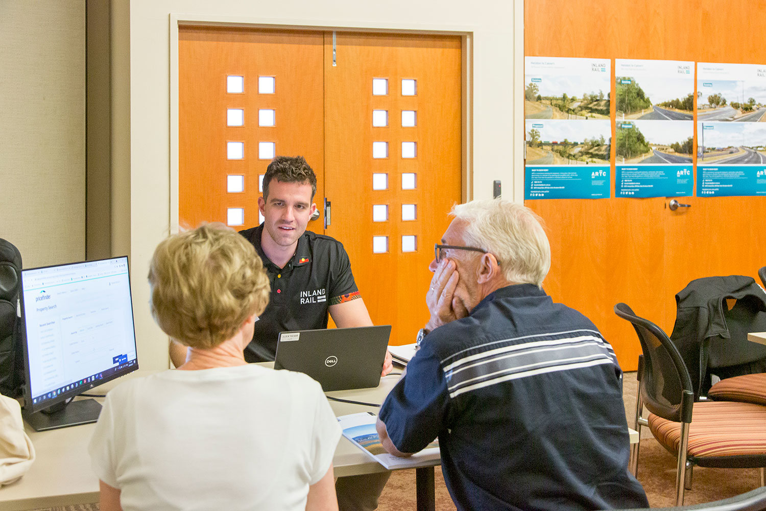 Image of an Inland Rail staff member talking to an elderly man and elderly woman.