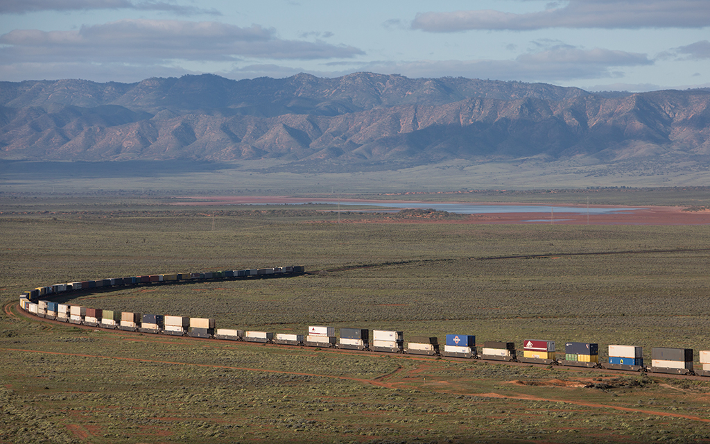 Double-stacked train travelling on an open plain with mountains in the background