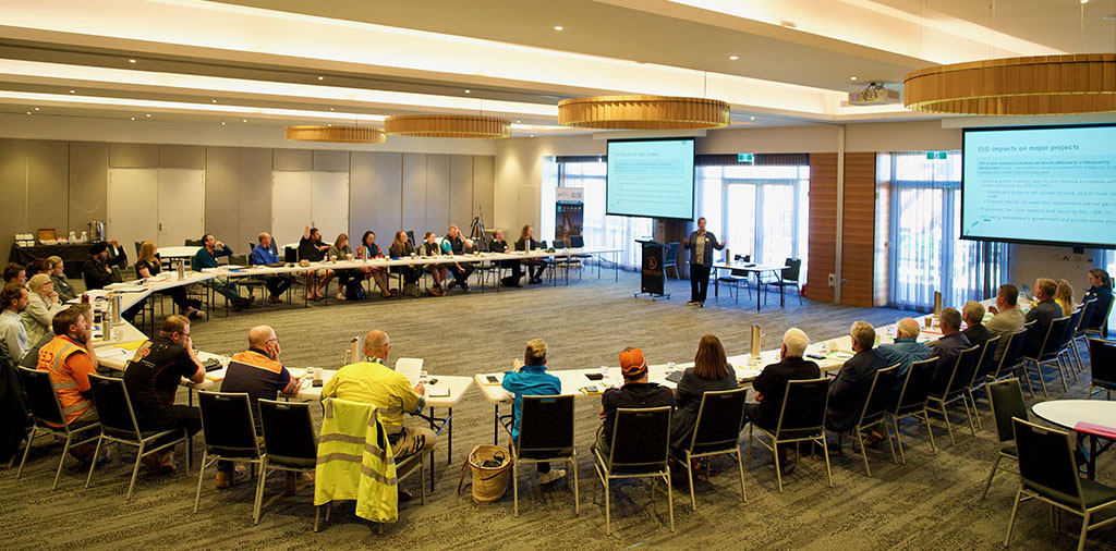 A conference room with people sitting around a u-shaped table listening to a lecturer.