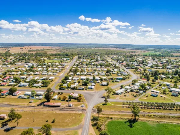 Aerial view of a small, rural town with forest and hills int he background, and a train line in the foreground.