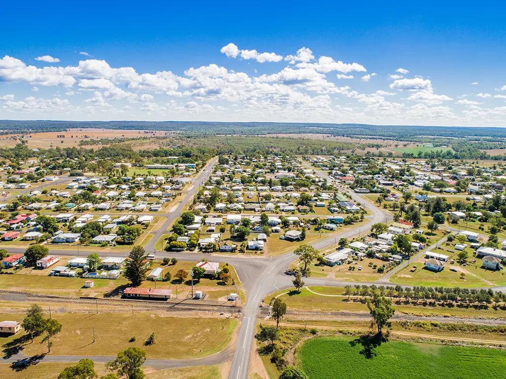 Aerial view of a small, rural town with forest and hills int he background, and a train line in the foreground.