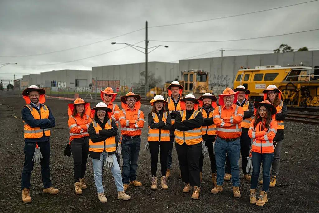 A group of people wearing high visibility safety gear standing in a rail yard.