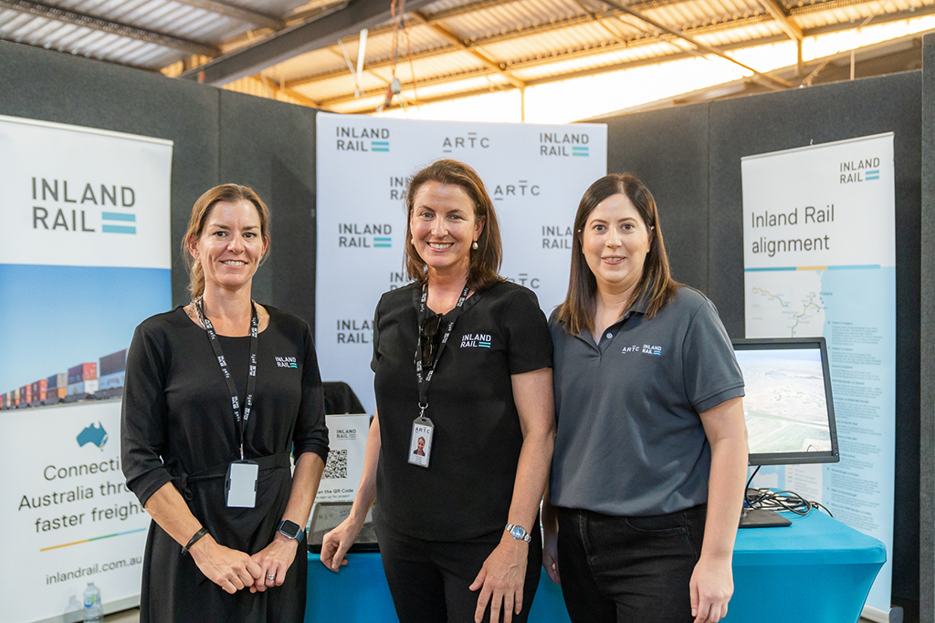 Three people standing in an information booth at a show.