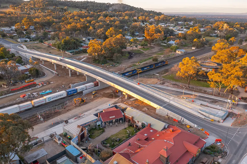 A freight train passes under a new bridge, in the middle of a construction site.