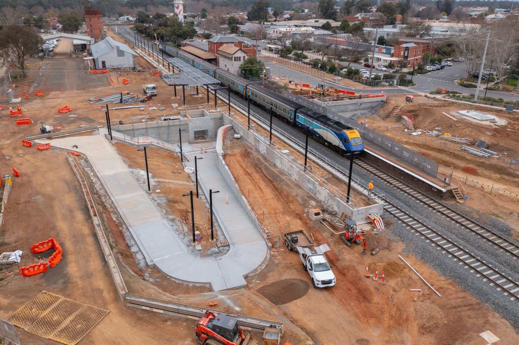 A worksite showing a curved concrete path next to a railway line, with a train on it.