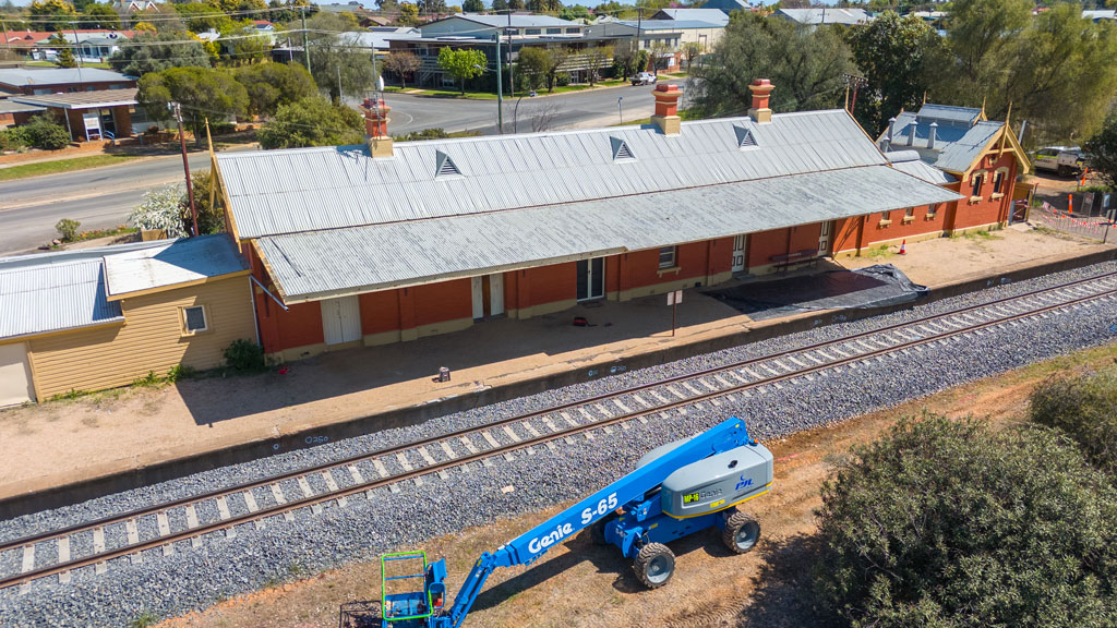 A heritage railway station building, platform and tracks, with a crane next to it.