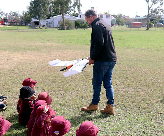 A man standing in a field with drone equipment in front of a seated group of students