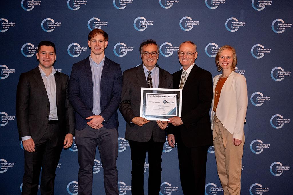 Five people in a row, with the middle person holding a certificate