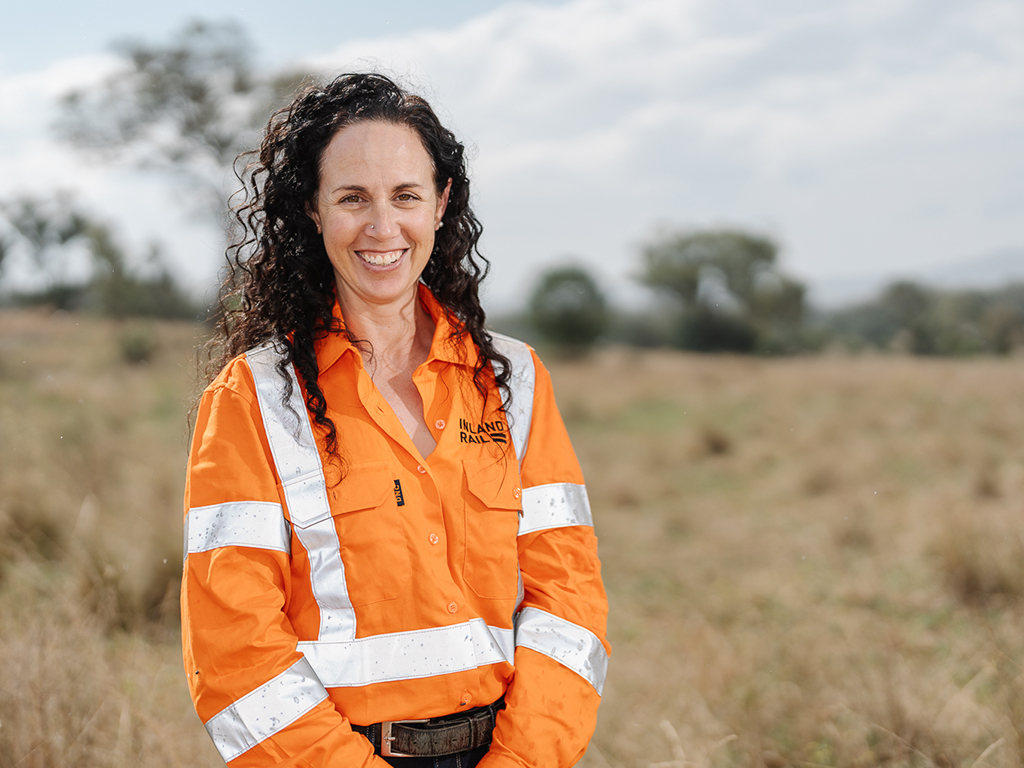 A woman standing facing the camera, smiling, wearing high visibility workwear in a field