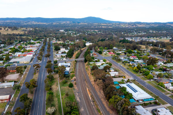 A drone shot of Broadford, showing, in the distance, a mountain range. In the foreground is a train station and road infrastructure around it.