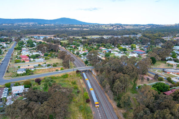 A train passes under a road bridge in a semi-rural setting.