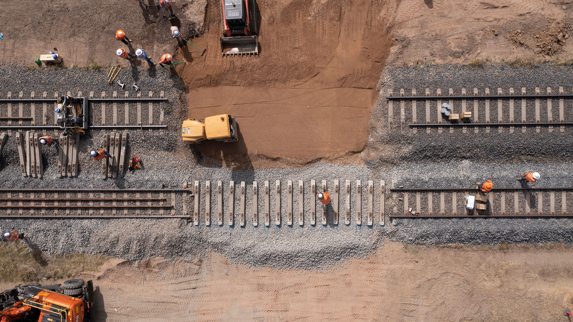 Workers and heavy machinery replace concrete sleepers along a section of railway track.