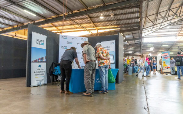 Three people leaning over a table with Inland Rail banners in the background