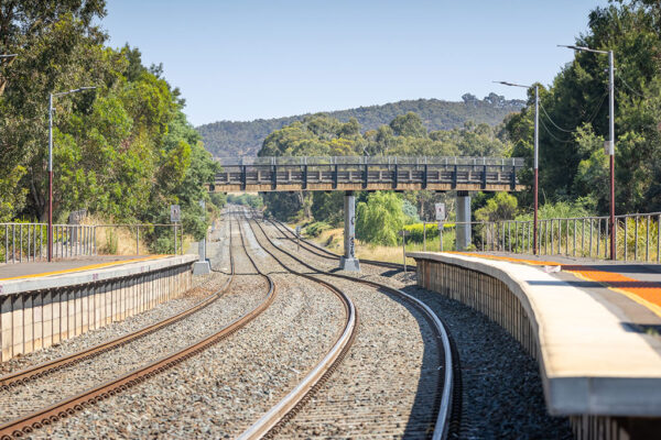 A car drives over a rail bridge in a rural setting.