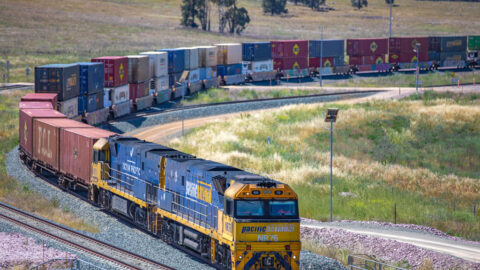 A train travels the curve in a track. The train has two containers stacked on top of each other.