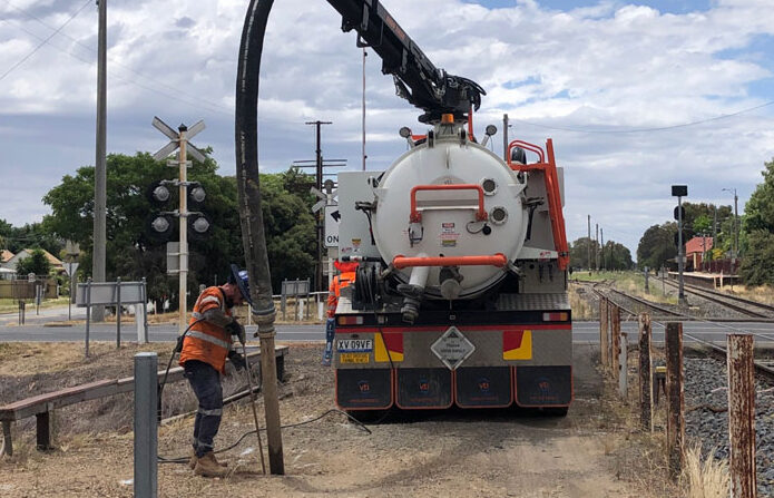 Beside a railway line, a truck with a long boom and hose is being attended to by a worker.