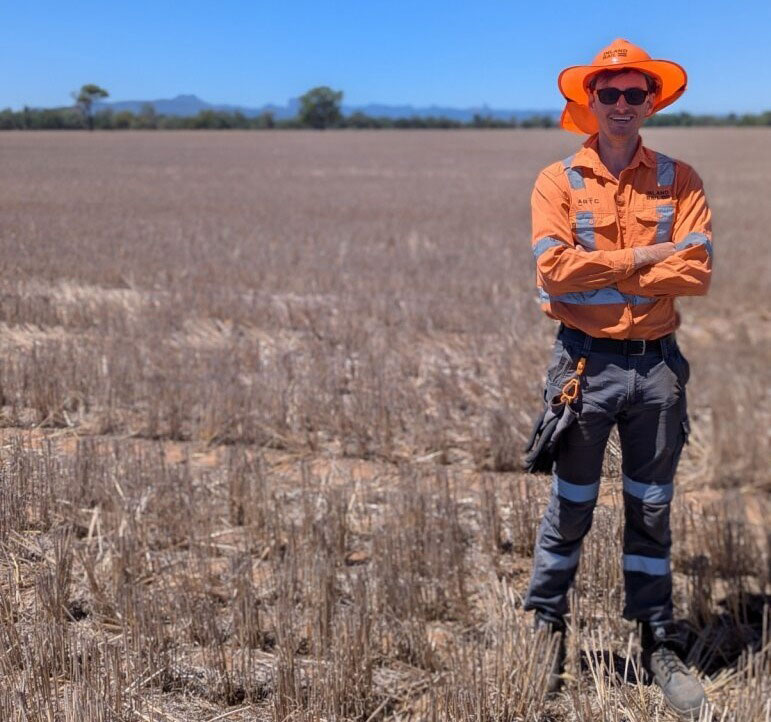 A man in high visibility work wear stands in a field of dry grass.