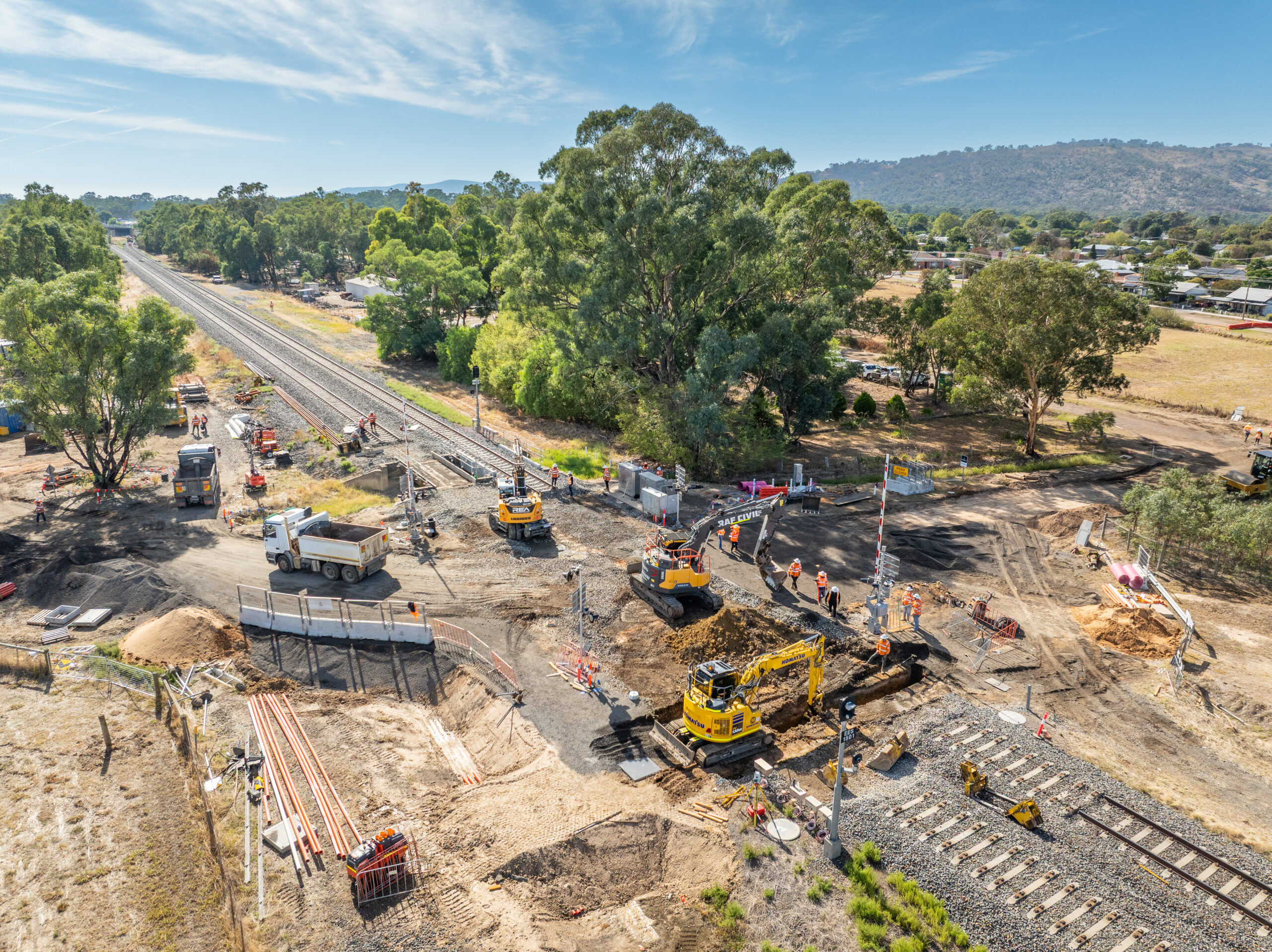 A busy work site across a rail line featuring earthmoving equipment and many workers.