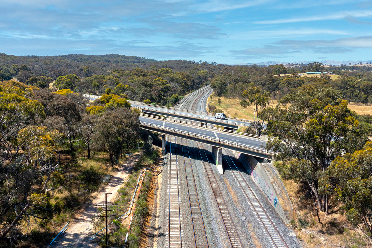 Two parallel road bridges cross over a rail corridor in a rural setting.