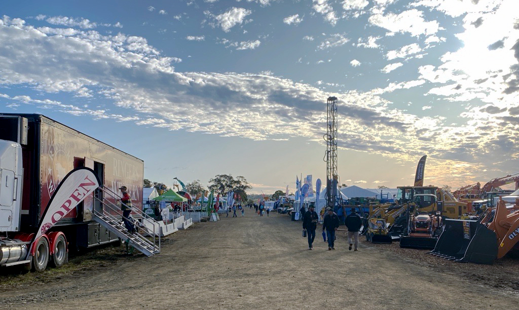 A dirt path with a truck on the left, heavy machinery on the right and people walking in the distance