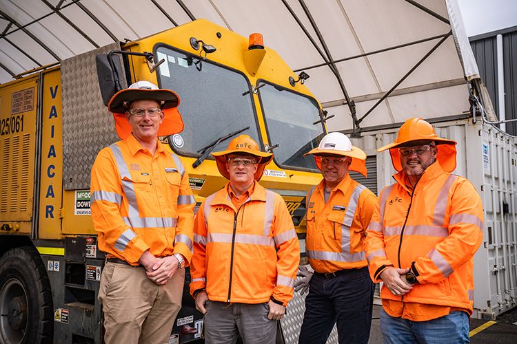 Four men wearing high-viz workwear smiling and standing in front of some yellow machinery