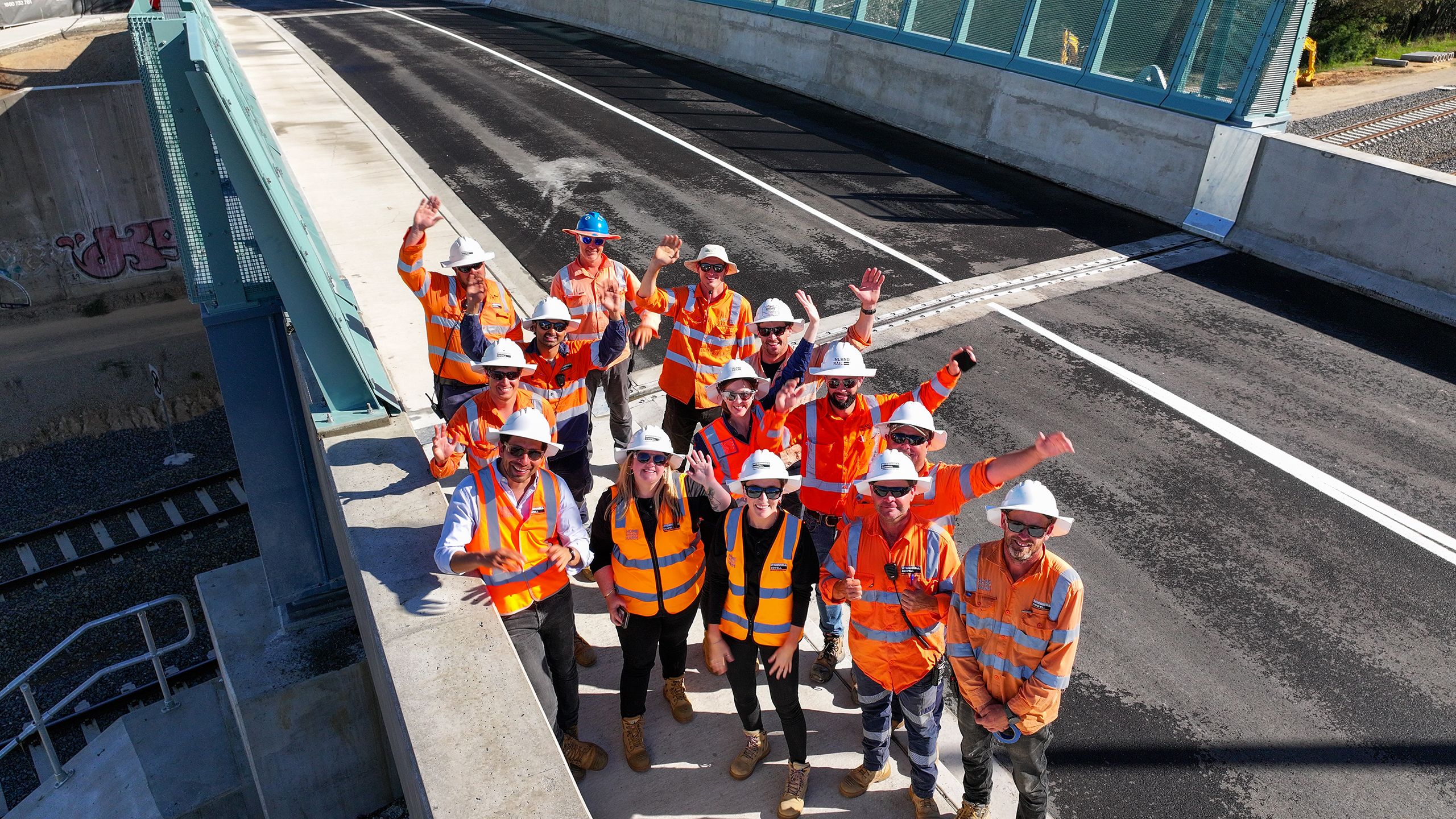 Group of people in high-viz workwear standing on a bridge waving and smiling