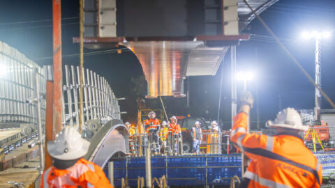 Construction workers installing a bridge section at night under bright lights.