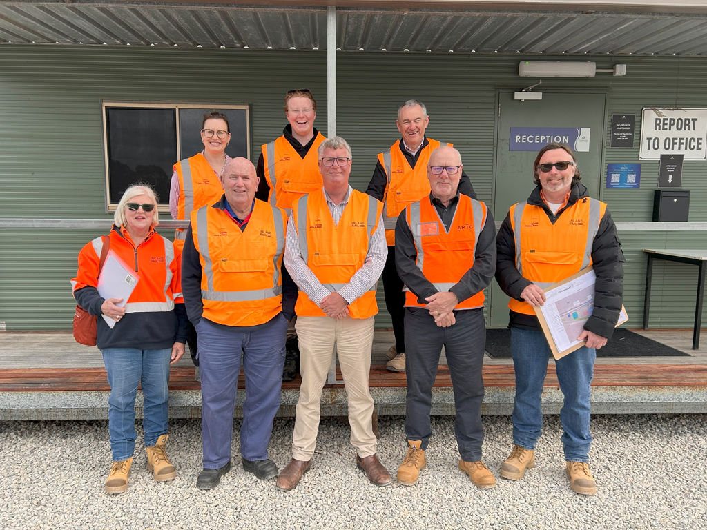 Eight people in high visibility vests stand outside a temporary building, with a reception sign in the background.