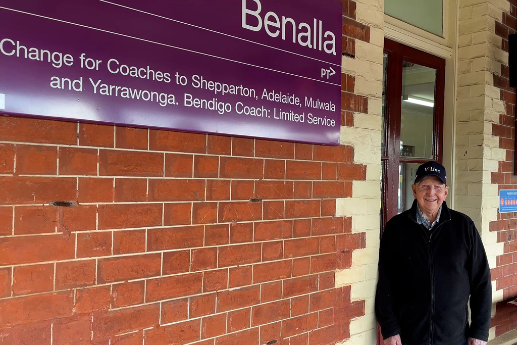 A man stands beside a railway station sign.