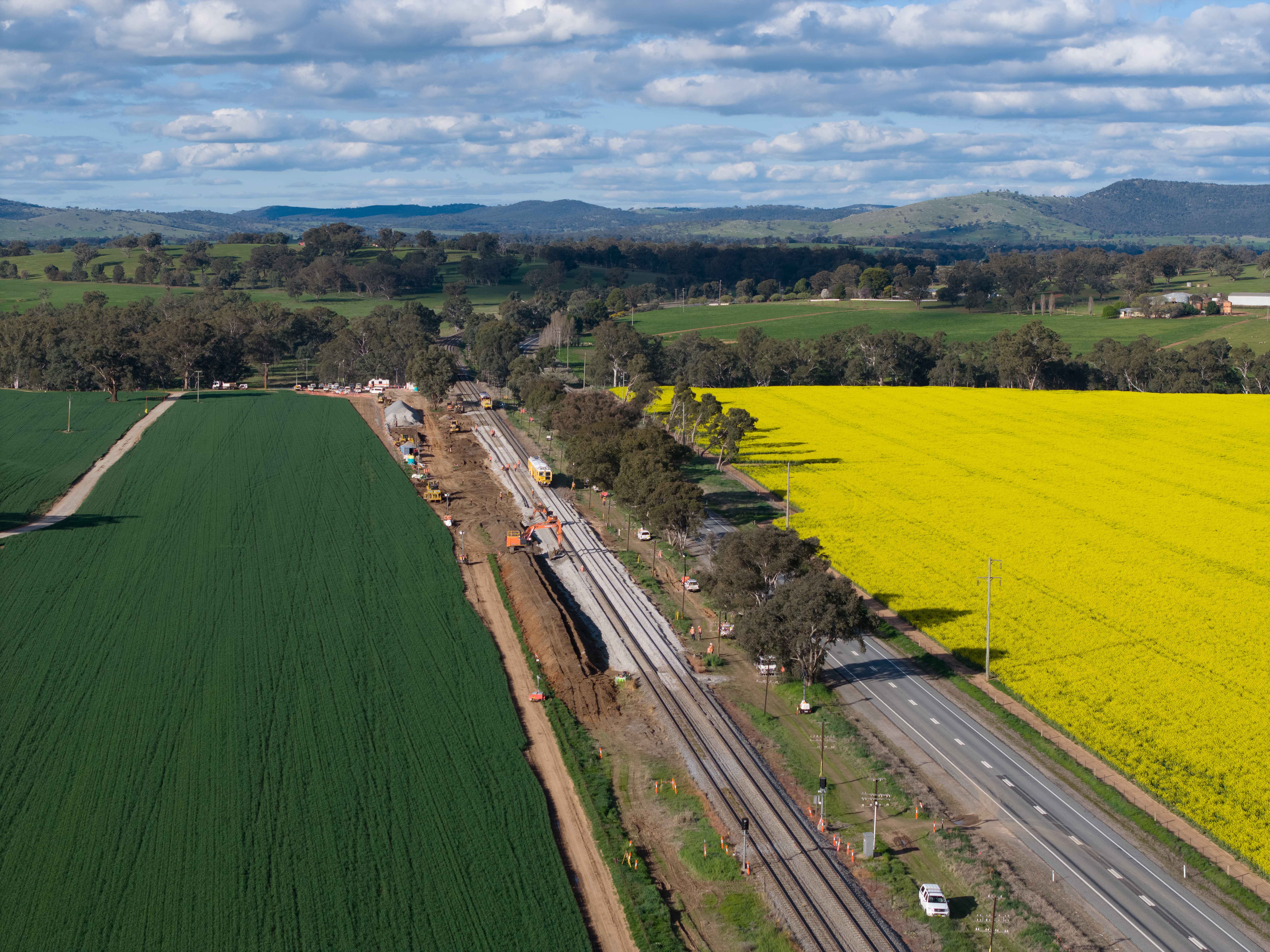 Fields of crops lie either side of a roadway and railway line.