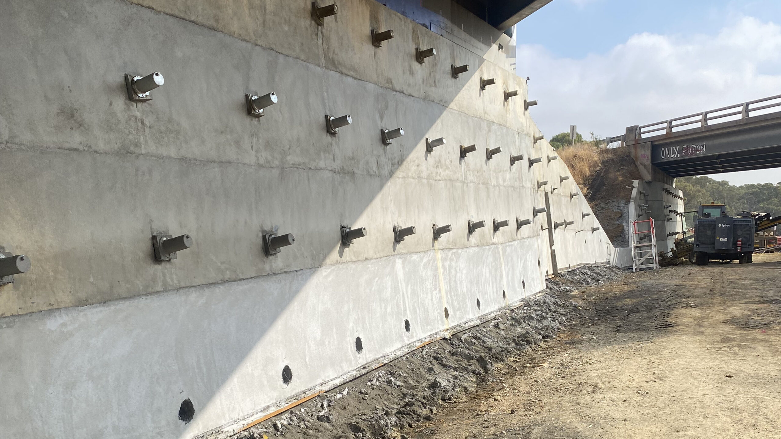 Soil nails installed in the retaining wall under a bridge, with excavation works in front.