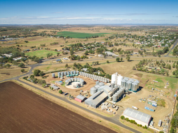 An aerial view of the rural township of Pittsworth. In the foreground is an agricultural/industrial site with many silos and large sheds.