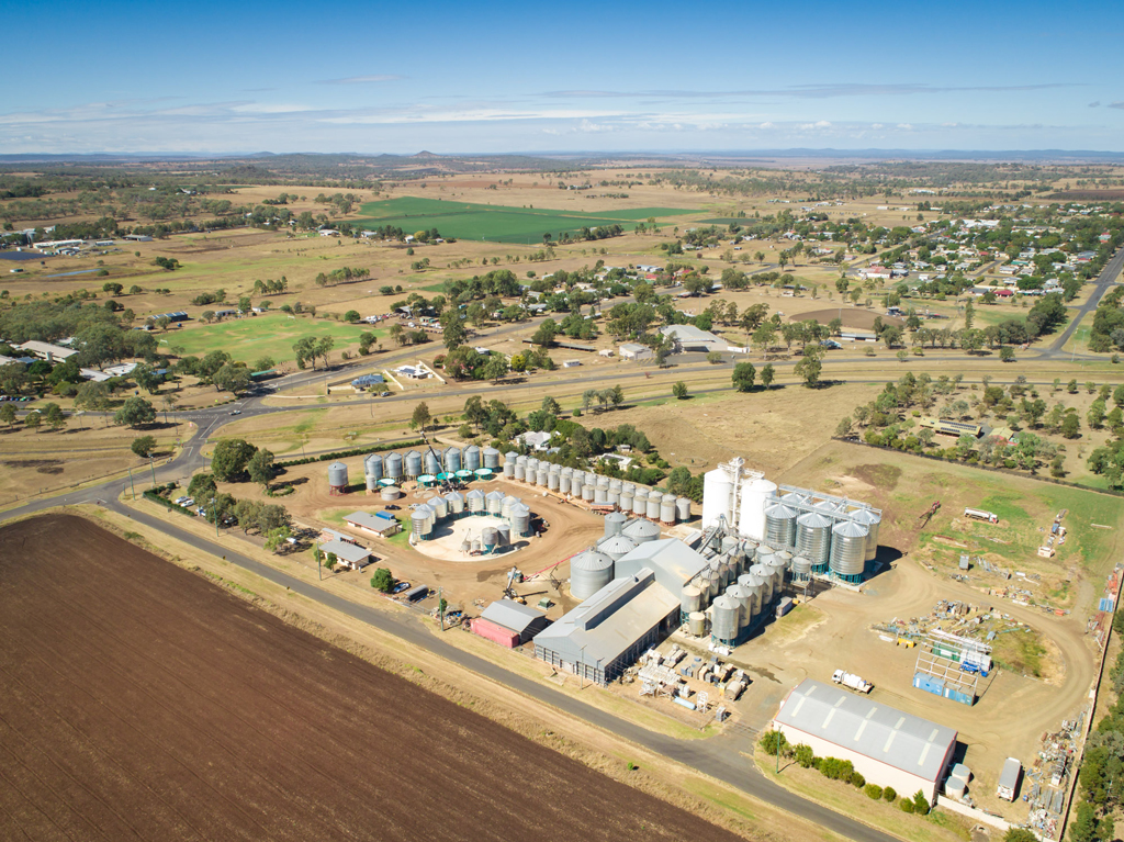 An aerial view of the rural township of Pittsworth. In the foreground is an agricultural/industrial site with many silos and large sheds.
