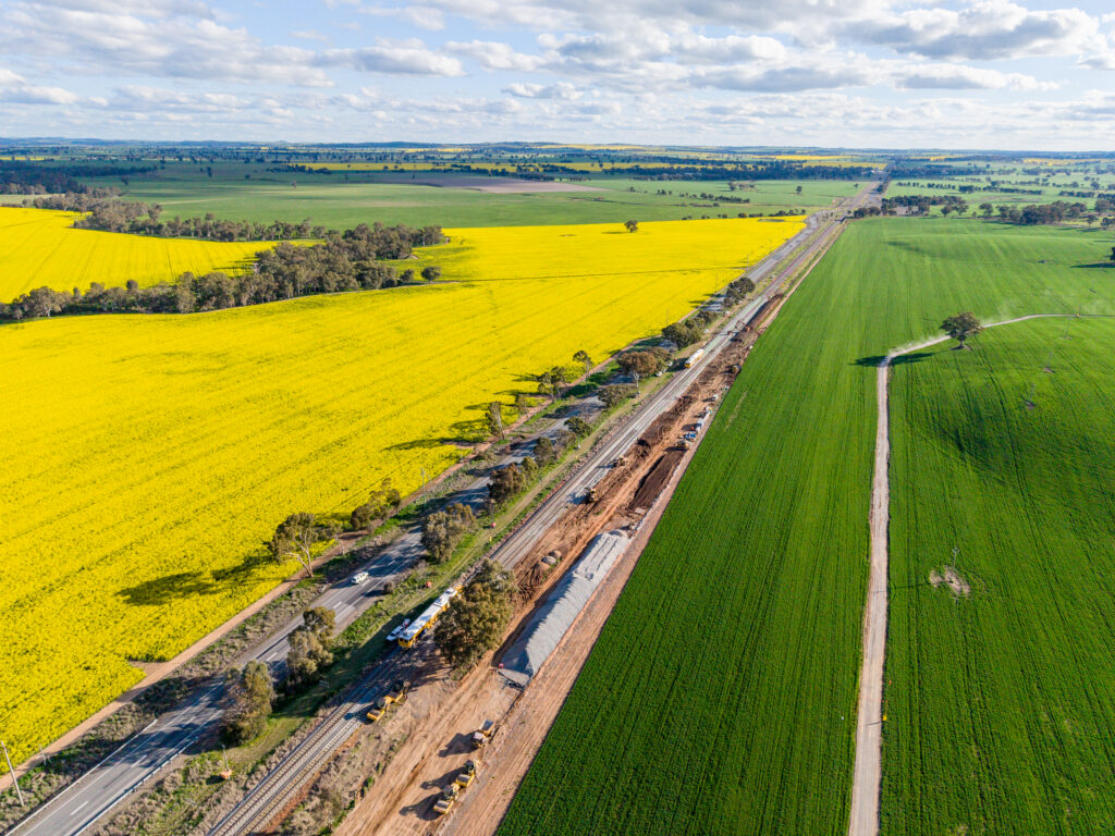 A rail line runs through fields to the horizon. Workers dot the rail line in one area.