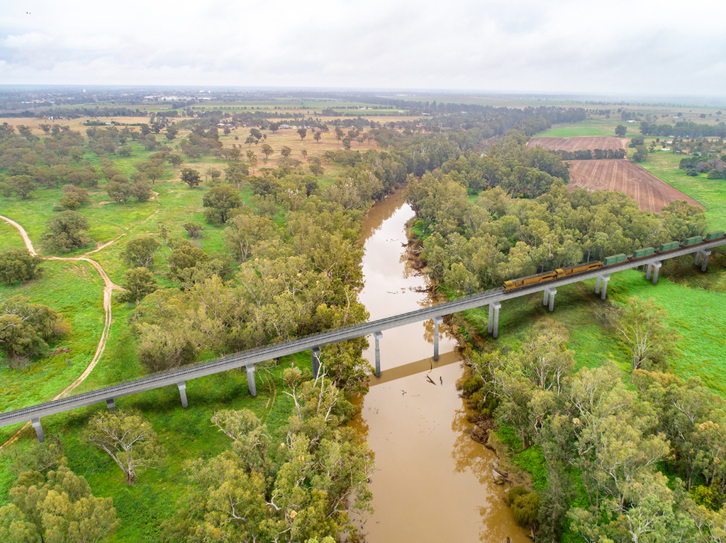 A train on a bridge crosses a river in a regional setting.