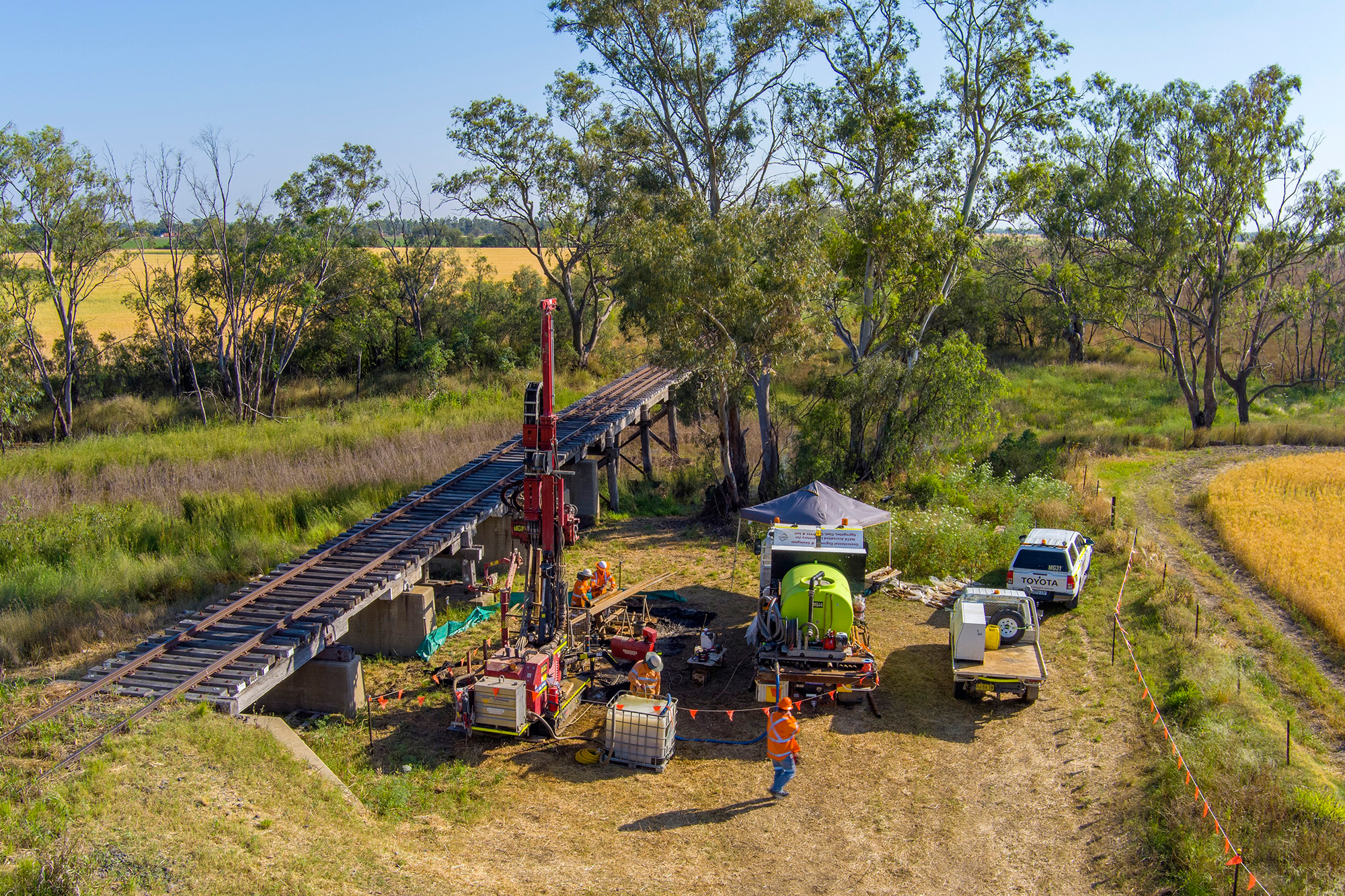 An old wooden rail bridge in a rural area, with a drill rig and worksite set up next to it.