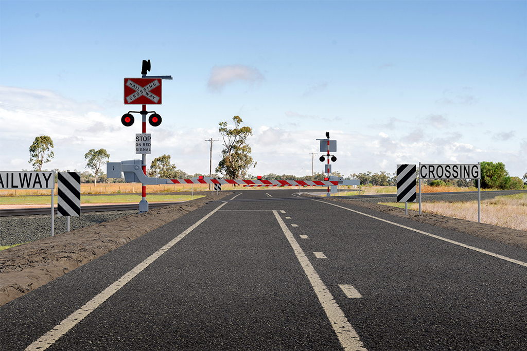A rural road leads to an intersection in a rural area. A railway crosses the road, and a level crossing signage and slights can be seen before each side of the railway facing oncoming traffic.