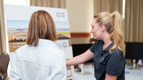 People discussing information displayed on a project board at an indoor community event.