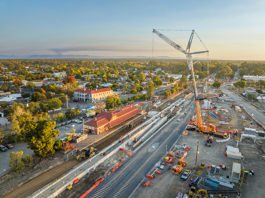 Early evening aerial view of rail works with a large crane near a station.
