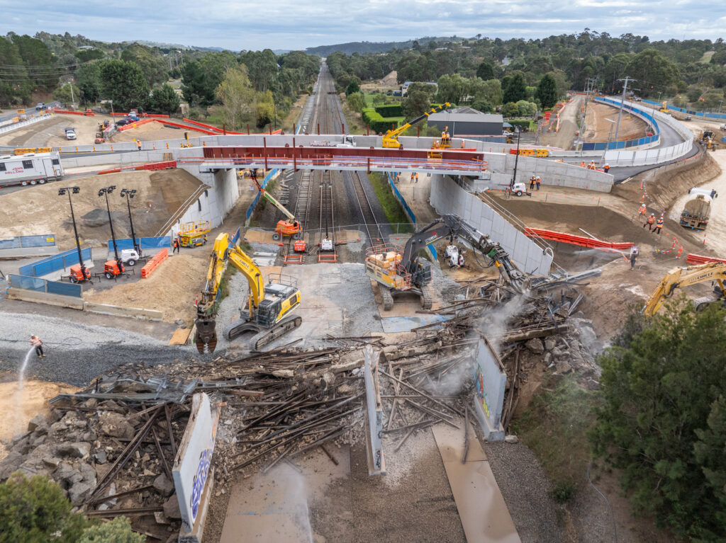 Excavators demolishing a bridge over railway tracks.