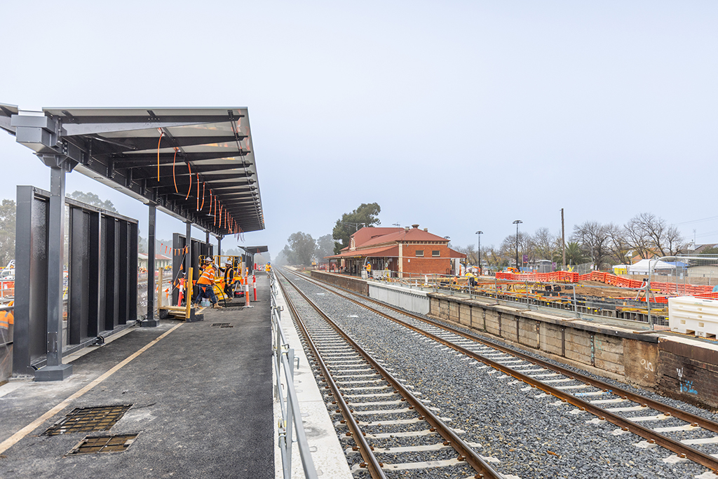 New platform canopy beside railway tracks with workers completing construction works.