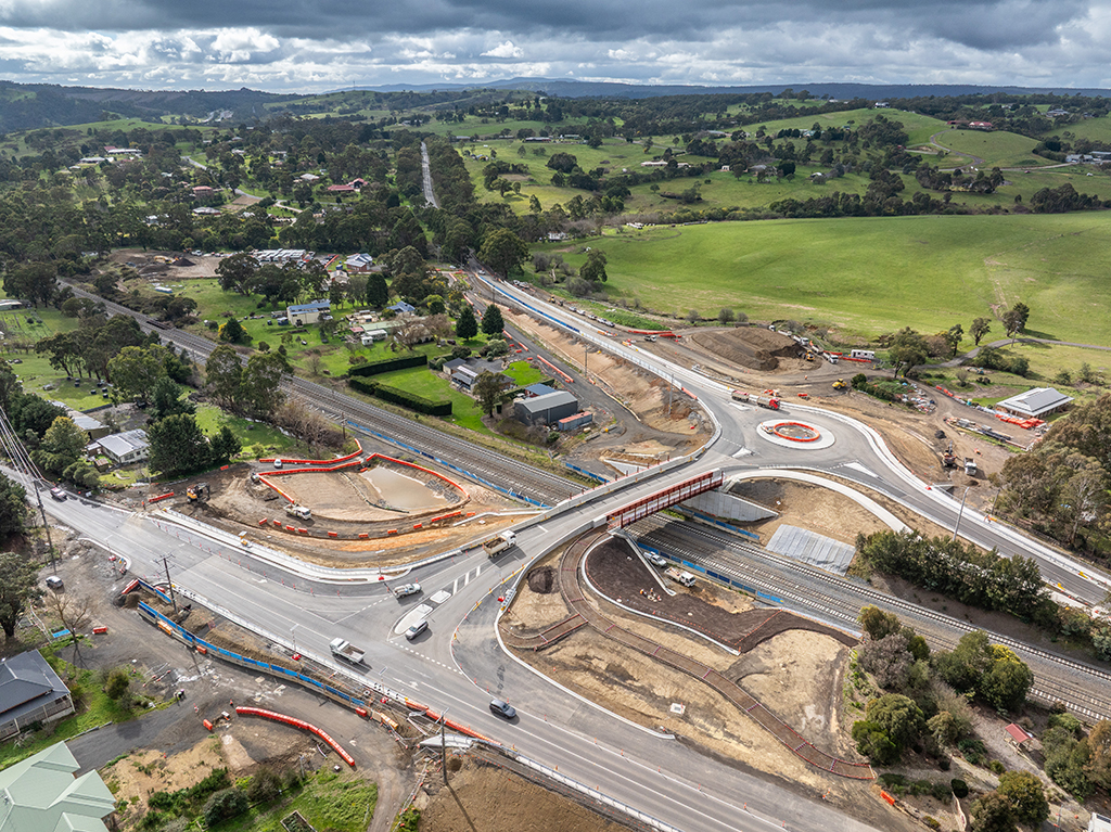 Aerial view of a road bridge over railway tracks with a roundabout and surrounding roads.