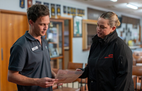Two people stand in a room talking about a flyer one person is holding.