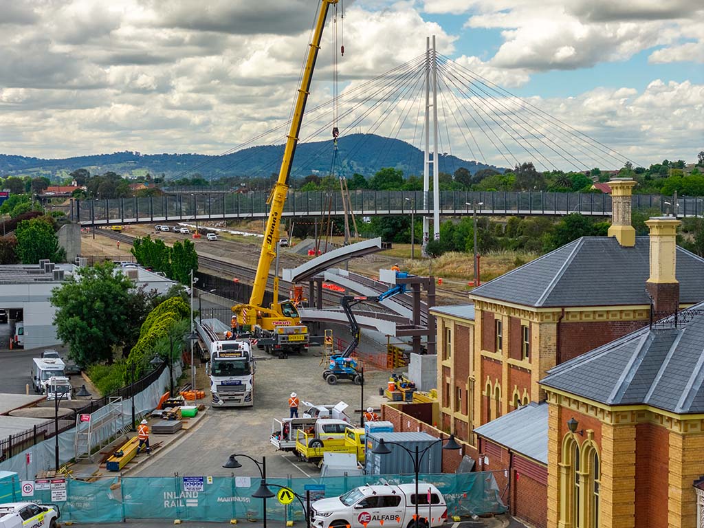 A crane lifts a large rectangular structure next to a rail line next to a heritage railway station.