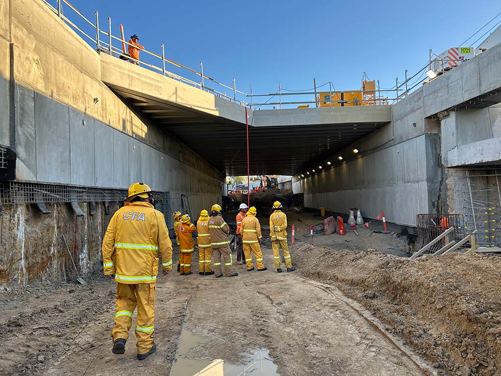 A small group of people in protective clothing stand in a worksite under a bridge.