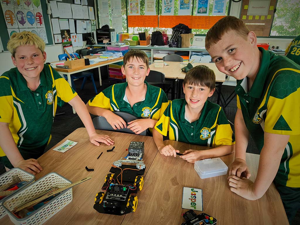 Four school students around a table with an electronic vehicle on it, which they are constructing.